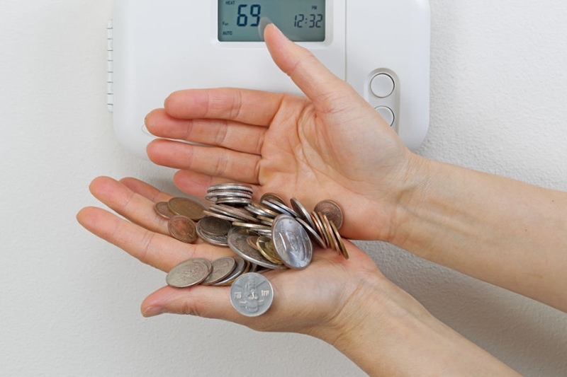 How to Save Money on AC - Hands Holding Coins Under a Thermostat.