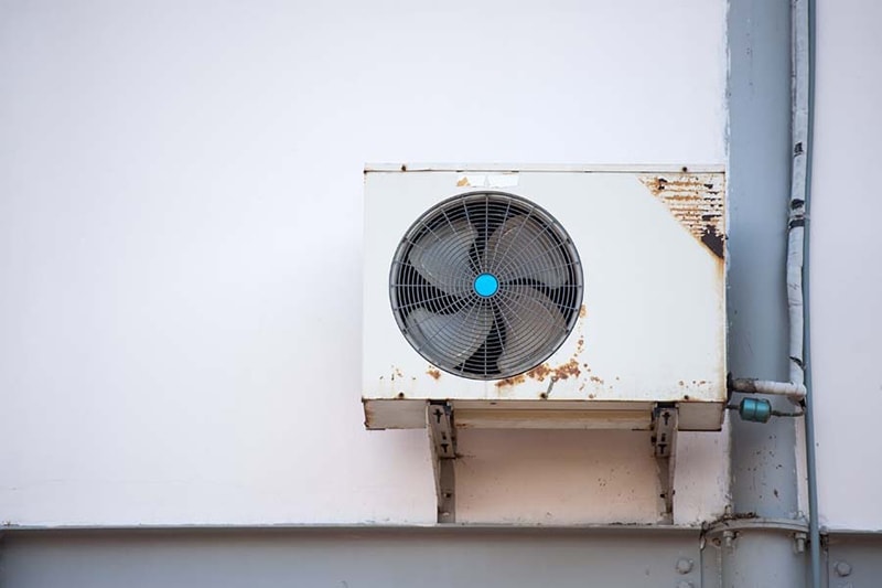 A rusty air conditioning unit set in a wall | 3 Telltale Signs It’s Time for a New AC | Clackamas