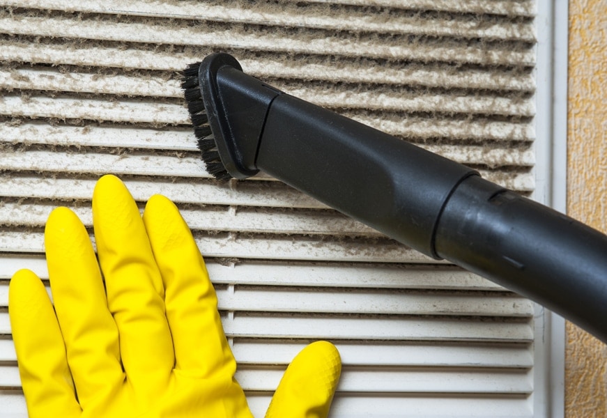 Air Handler Maintenance. Hand in yellow glove and vacuum cleaner pipe. Ventilation grill cleaning.