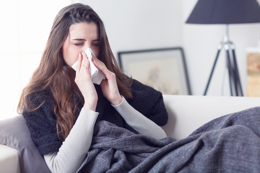 Young attractive woman lying sick at home couch in cold and flu sneezing nose with tissue covering with blanket. ﻿What Indoor Air Quality Accessories Can Help Keep Me Healthy?